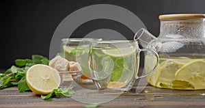 putting brown sugar into cup with natural organic herbal tea with lemon and mint with glass teapot on a wooden table