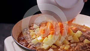 Putting chopped carrot into the roux in frying pan with beef and potato.