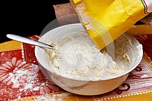 Putting flour from paper bag into bowl with dough