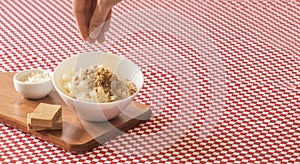 Putting pacoca sweet on brazilian dessert canjica of white corn with in bowl and towel. Festa Junina Party Brazilian Culture