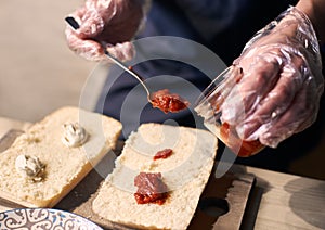 Putting sauce with spoon over big bread pieces for preparing nourishing sandwich by traditional Italian recipe. Close up