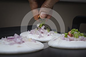 putting sliced capsicum on mini round white utappam with fingers