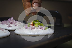 Putting sliced capsicum on utappa and onions with fingers