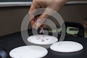 putting sliced onions on mini round white utappam with fingers