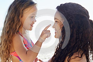 Putting on sunblock. A young girl poking her mothers nose while theyre at the beach.