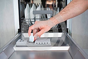 Putting tab into dishwasher, close up. A man hand holding dishwasher detergent tablet. Dishwasher machine full loaded