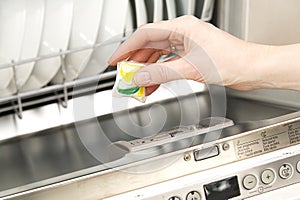 Putting tab into full integrated dishwasher close up. dishwasher machine full loaded. woman hand holding dishwasher