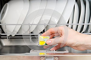 Putting tab into full integrated dishwasher close up. dishwasher machine full loaded. woman hand holding dishwasher