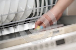 Putting tab into full integrated dishwasher close up. dishwasher machine full loaded. woman hand holding dishwasher