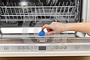 Putting tab into integrated dishwasher close up. dishwasher machine full loaded. woman hand holding dishwasher detergent tablet