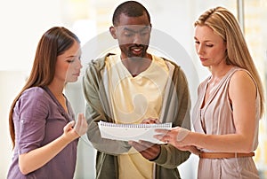 Putting their heads together. three business professionals standing and going through some paperwork together.