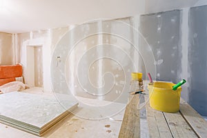 Putty knife, yellow buckets with glue and glue rollers on the wooden board in room is under construction