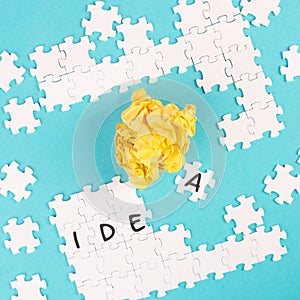 Puzzle on a blue background, yellow crumbled paper, word idea is standing on the jigsaw pieces, brainstoming concept, working