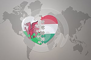 puzzle heart with the national flag of hungary and wales on a world map background.Concept