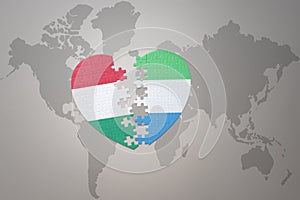 puzzle heart with the national flag of sierra leone and hungary on a world map background.Concept