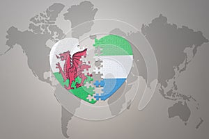 puzzle heart with the national flag of sierra leone and wales on a world map background.Concept