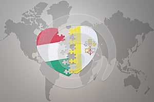 puzzle heart with the national flag of vatican city and hungary on a world map background.Concept