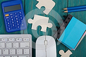 Puzzle pieces, calculator, sketchbook, computer keyboard on a blue wooden background