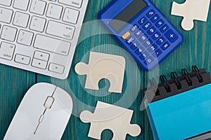 Puzzle pieces, calculator, sketchbook, computer keyboard and mouse on blue wooden background
