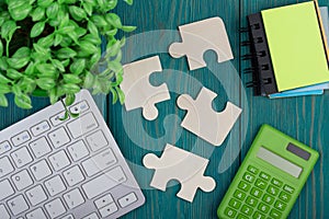 Puzzle pieces, calculator, sketchbook, computer keyboard on wooden background