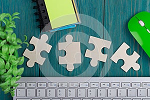 Puzzle pieces, sketchbook, computer keyboard and mouse on blue wooden background