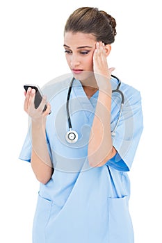 Puzzled brown haired nurse in blue scrubs using a mobile phone