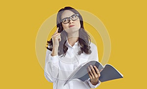 Puzzled brunette woman student in glasses thinking looking up with pen and copybook in hands.