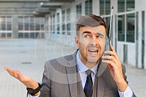 Puzzled businessman using obsolete wireless phone with antenna