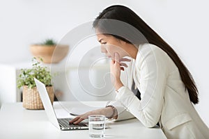 Puzzled confused asian woman thinking hard looking at laptop scr