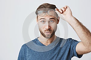 Puzzled and confused male student with stubble dressed in blue t-shirt, looking at camera with blue eyes, thinking about