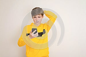 Puzzled, confused teenager boy in yellow hoodie sweatshirt with smartphone
