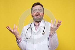 Puzzled doctor with a stupid expression on face and glasses on forehead, makes a confused gesture with hands. Yellow