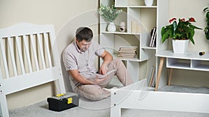 A puzzled father studies a complex instruction for assembling a children's bed.