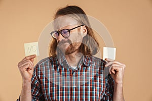 Puzzled ginger man showing piece of paper with yes and no signs