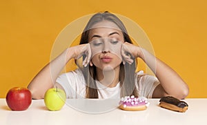 Puzzled Girl Choosing Healthy And Unhealthy Food, Leaning On Table