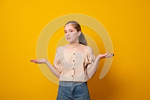 Puzzled girl, spreads hands with doubt,over yellow background. Teen girl faces dilemma