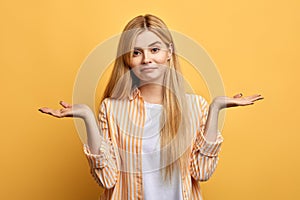 Puzzled hesitant girl with long fair hair with raised arms looking at the camera