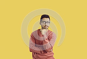 Puzzled male student in glasses isolated on yellow background thinking about something