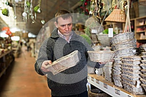 Puzzled man choosing wickerwork in shop