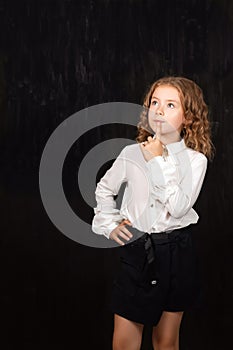 Puzzled schoolgirl girl ponders looking up at black place with copy space