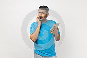 Puzzled thoughtful man holding chin and using tablet, looking away, trying to remember password.