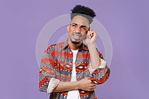 Puzzled tired young african american guy in casual colorful shirt posing isolated on violet wall background studio