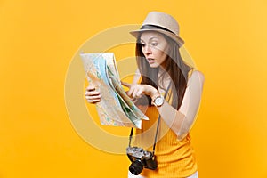 Puzzled traveler tourist woman in summer casual clothes, hat looking on city map isolated on yellow orange background