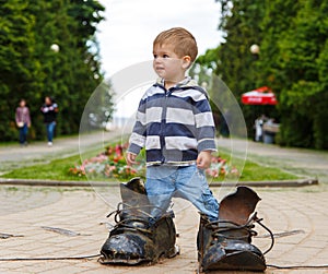 Puzzled two years old boy standing in giant boots