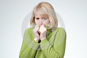 Puzzled woman with blonde hair feeling fear, keeping hands near cheeks, looking with amazement