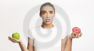 Puzzled Woman Holding Apple And Doughnut Choosing, Studio Shot, Panorama