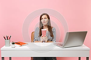 Puzzled woman in perplexity croaking thinking looking up holding plactic cup with cola, soda sit work at white desk with