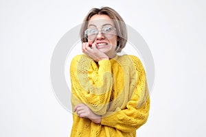 Puzzled woman in yellow sweater, keeping hands on cheeks, looking with fear, receiving bad news