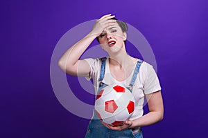 Puzzled young girl football fan watching match support favorite team with soccer ball, isolated on blue background.