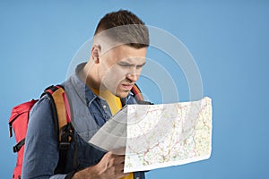 Puzzled young guy with tourist backpack and map over blue studio background